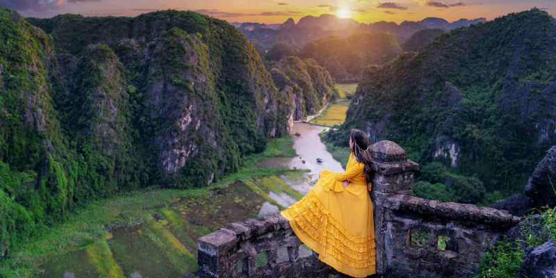 1.-woman-in-a-yellow-dress-enjoying-the-view-from-a-stone-lookout-at-mua-cave-with-a-valley-below..jpg